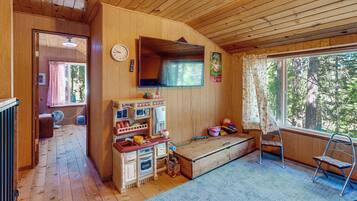 A wooden cabin interior with a kitchen area, a large window, and a view of the outdoors.