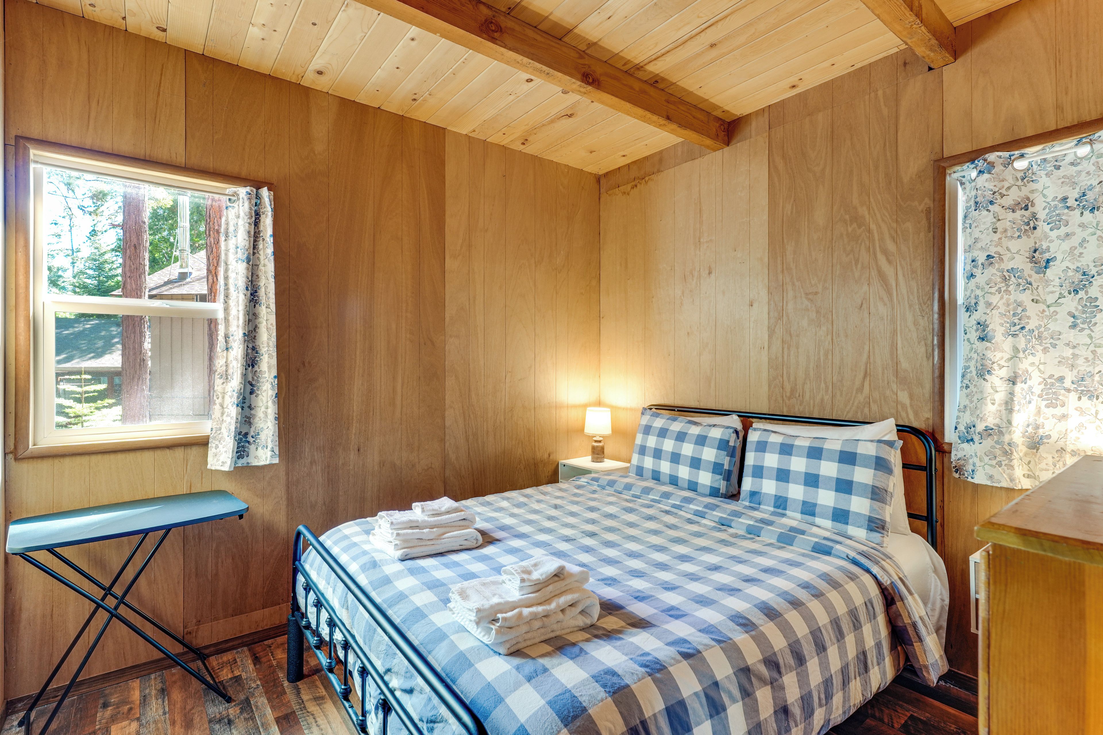 A bedroom with a bed, a nightstand, a lamp, a window with curtains, and a small table.