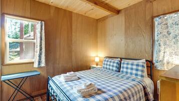 A bedroom with a bed, a nightstand, a lamp, a window with curtains, and a small table.