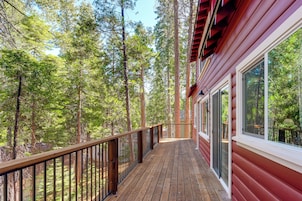 Une terrasse en bois avec une rambarde en métal, entourée de grands arbres.