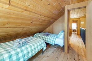 A room with two beds, wooden walls, and a sloped ceiling.