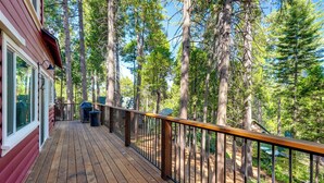 A wooden deck with a railing, overlooking a forested area.
