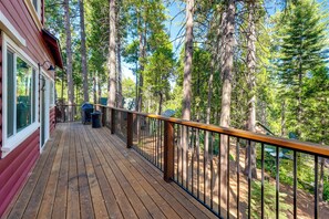 A wooden deck with a railing, overlooking a forested area.