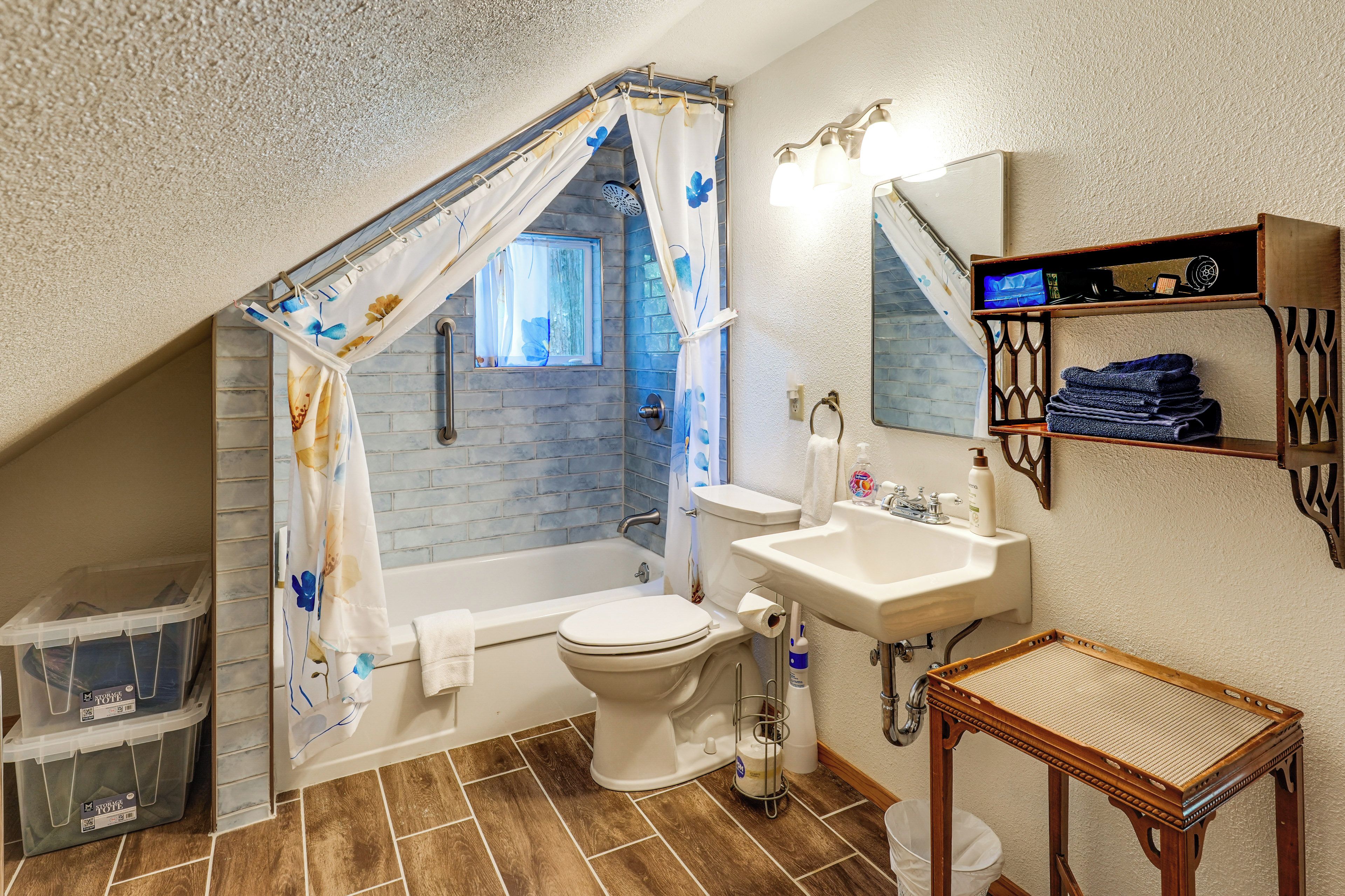 A bathroom with a shower curtain, a toilet, a sink, and a small table.