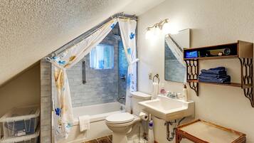 A bathroom with a shower curtain, a toilet, a sink, and a small table.