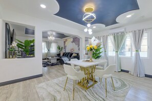 Una sala de estar moderna con comedor, que cuenta con una araña, un conjunto de sofás y un amplio ventanal con cortinas.