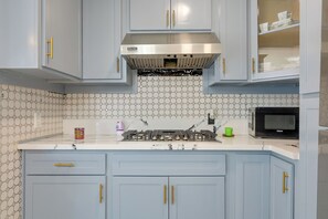 Una cocina con gabinetes azul claro, una campana extractora de acero inoxidable, un microondas y un salpicadero de azulejos hexagonales.