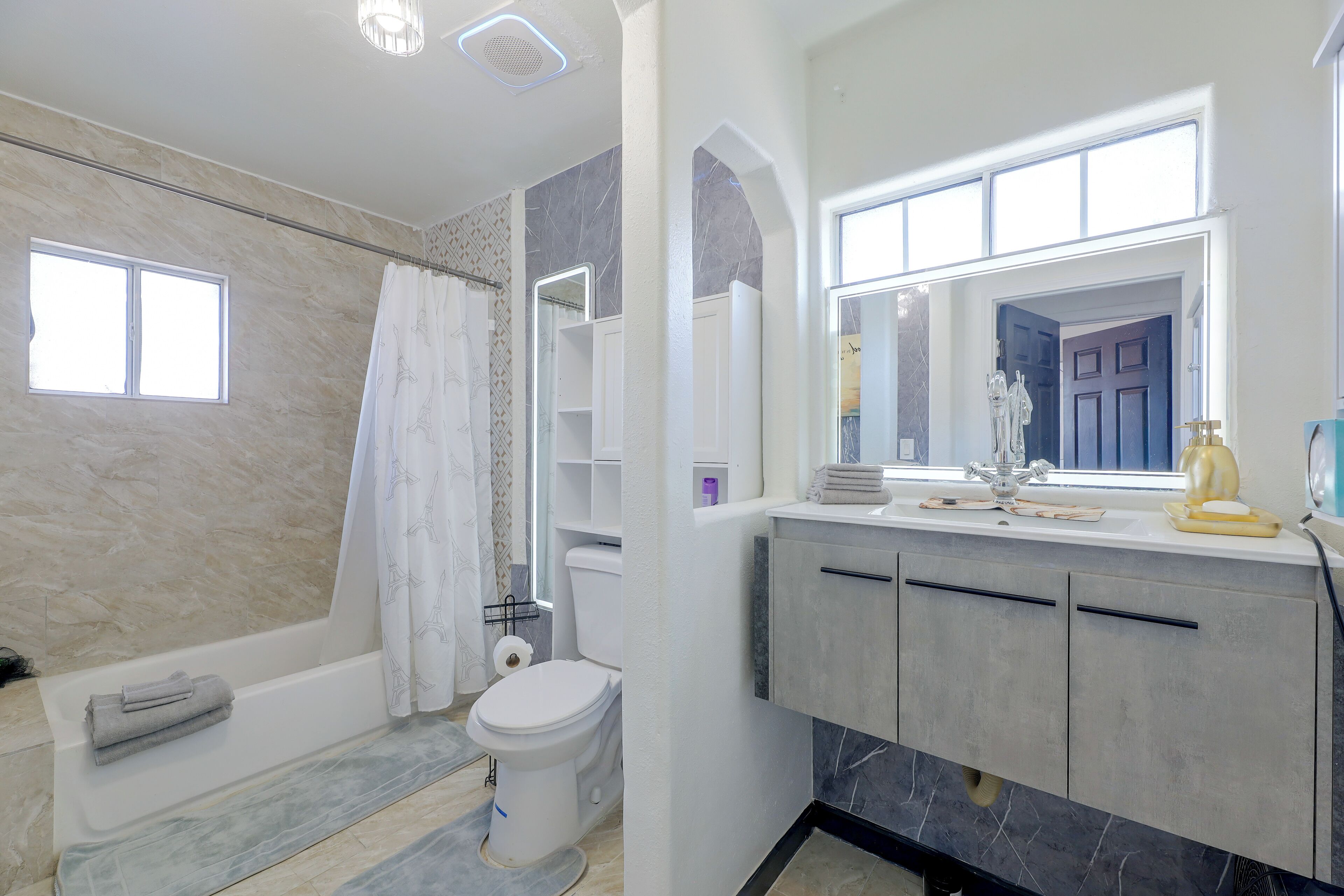 A bathroom with a bathtub, toilet, vanity with a mirror, and a window.