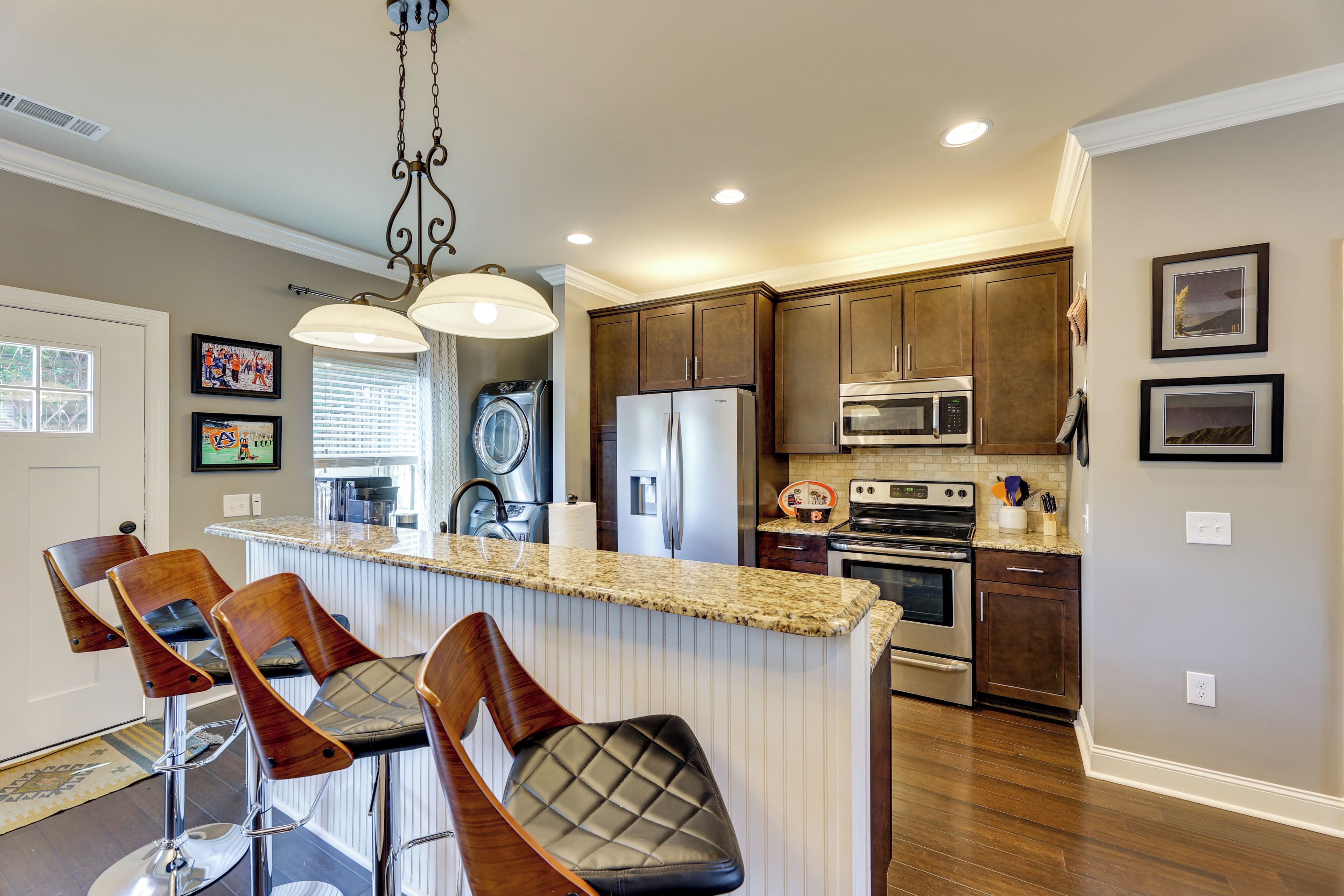 A kitchen with a central island, bar stools, a refrigerator, an oven, and a microwave.