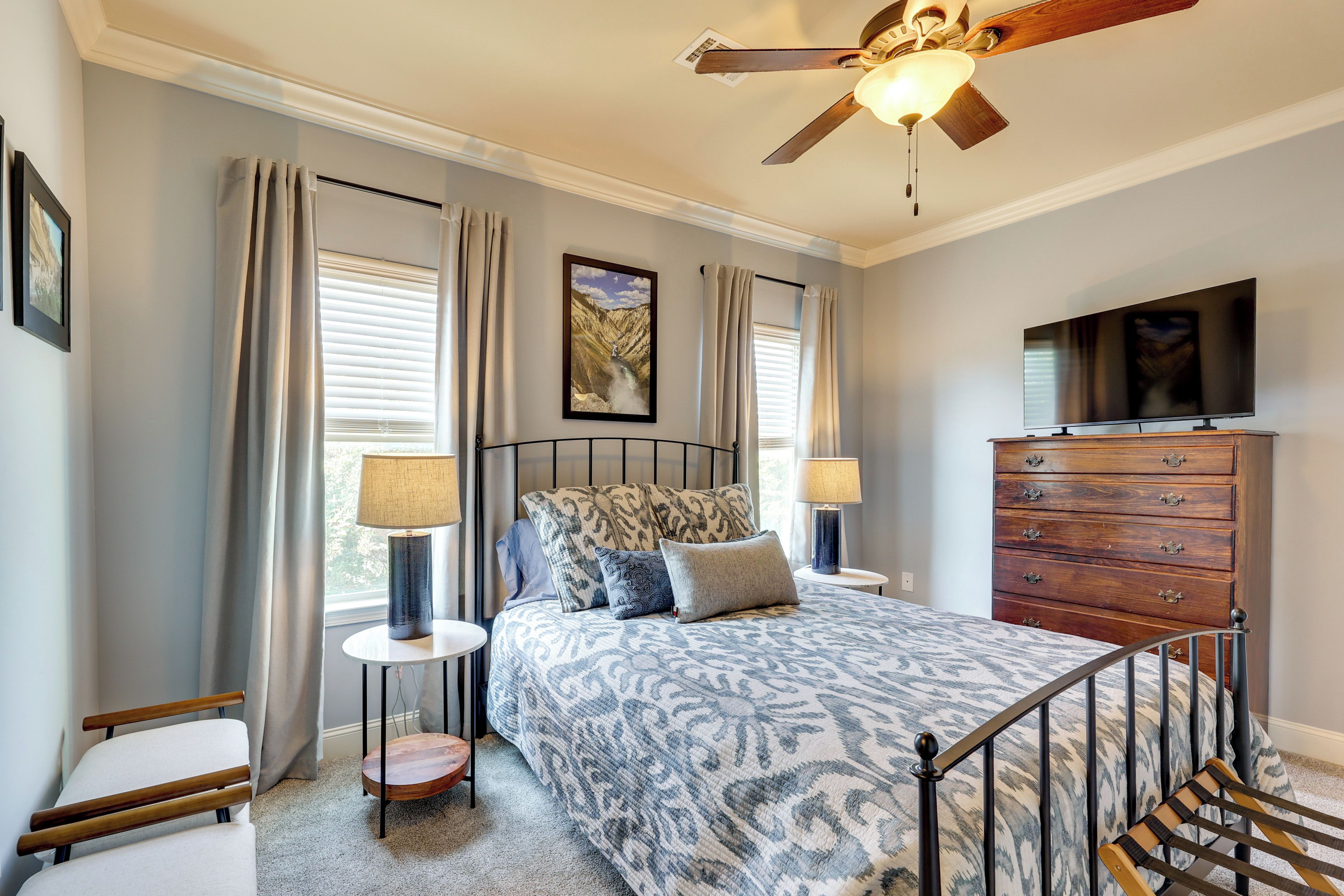 A bedroom with a bed, a dresser, a television, and a ceiling fan.