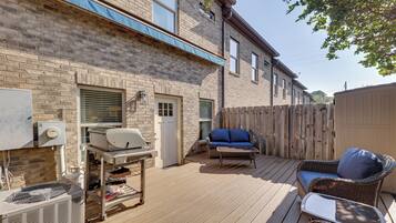 A patio with a grill, outdoor furniture, and a brick building in the background.
