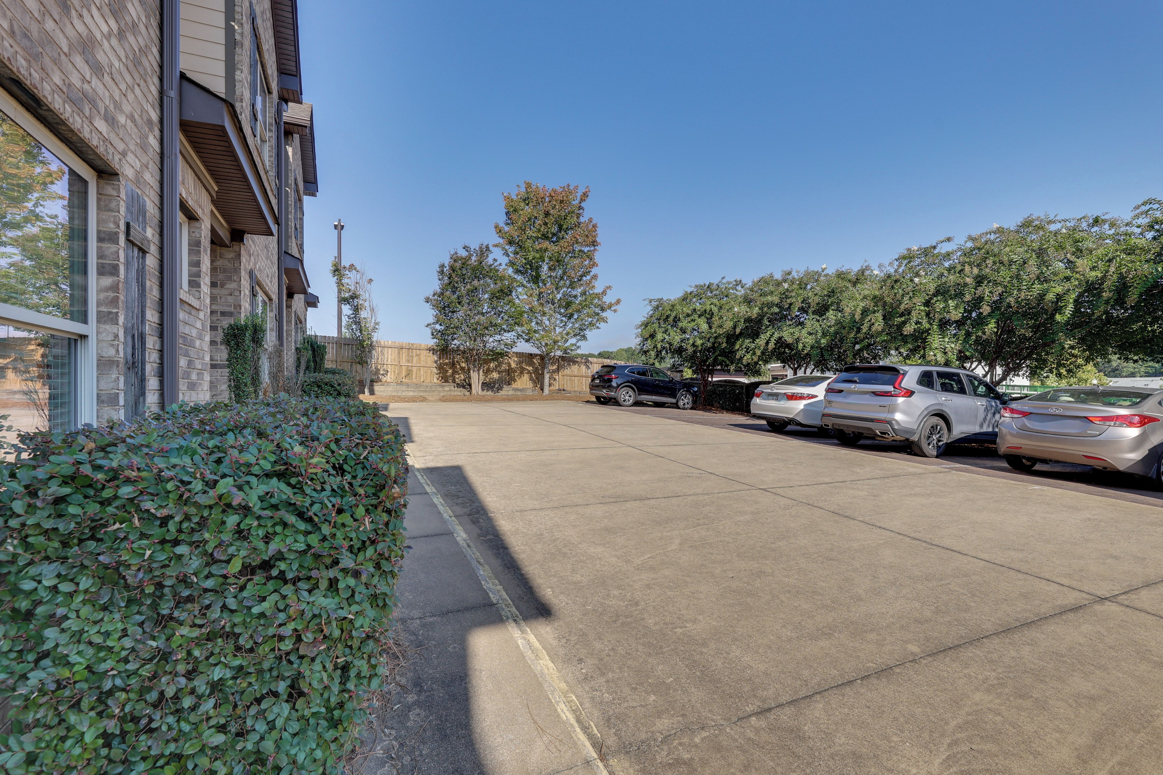 A parking lot with several cars, a building with a brick facade, and a hedge.