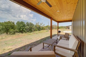 Un patio cubierto con mobiliario exterior, vista a un área verde y un edificio al fondo.