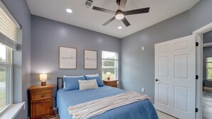 Un dormitorio con cama, ventilador de techo, dos luces fijadas a la pared, una ventana con persianas y una puerta.