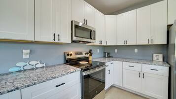 A modern kitchen with white cabinetry, a stainless steel stove, and a microwave.