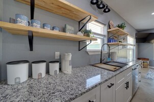 Una cocina con encimeras de granito, armarios blancos y repisas de madera.