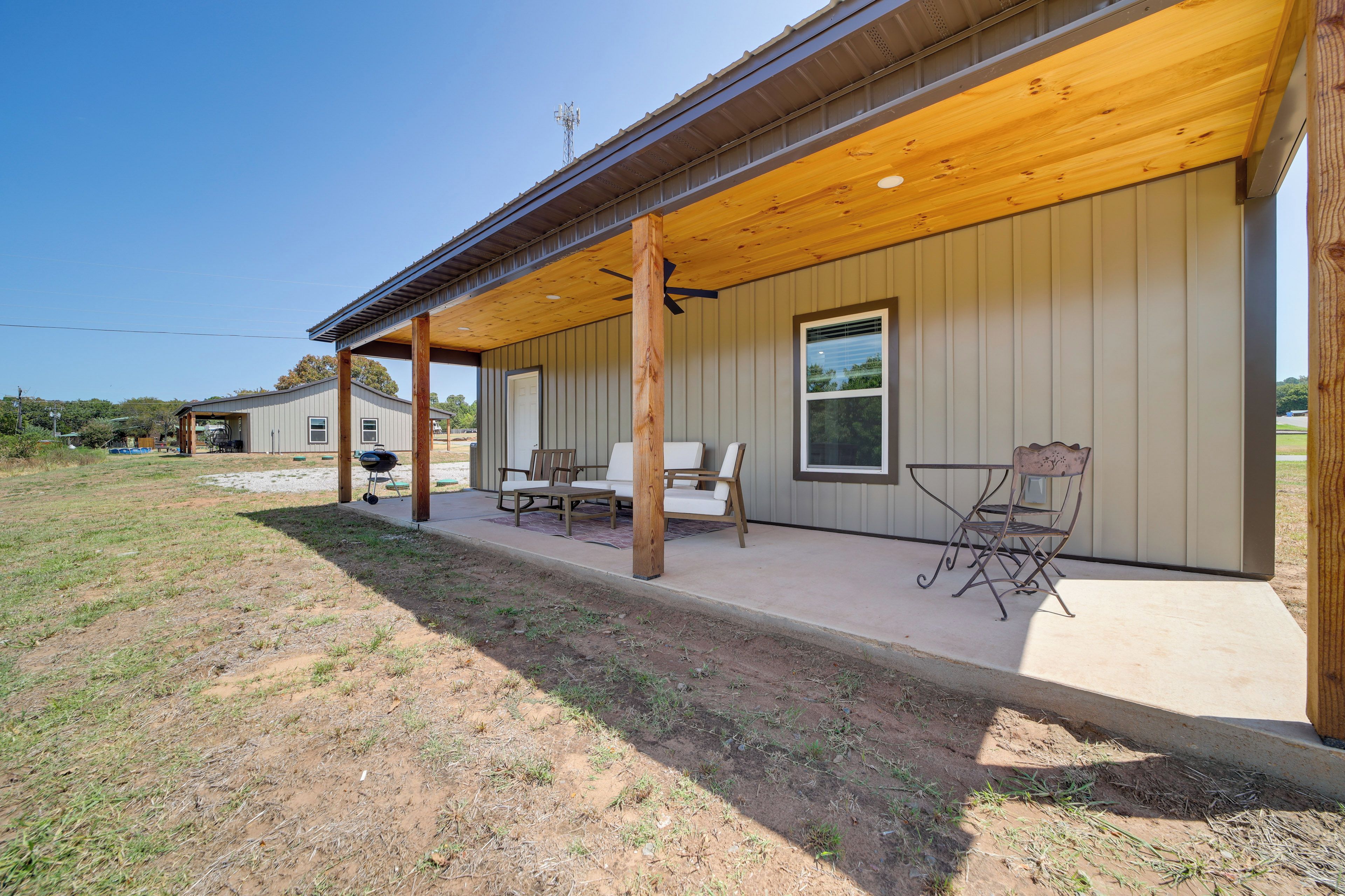 A covered outdoor area with a table and chairs, a barbecue grill, and a building with a window and door.