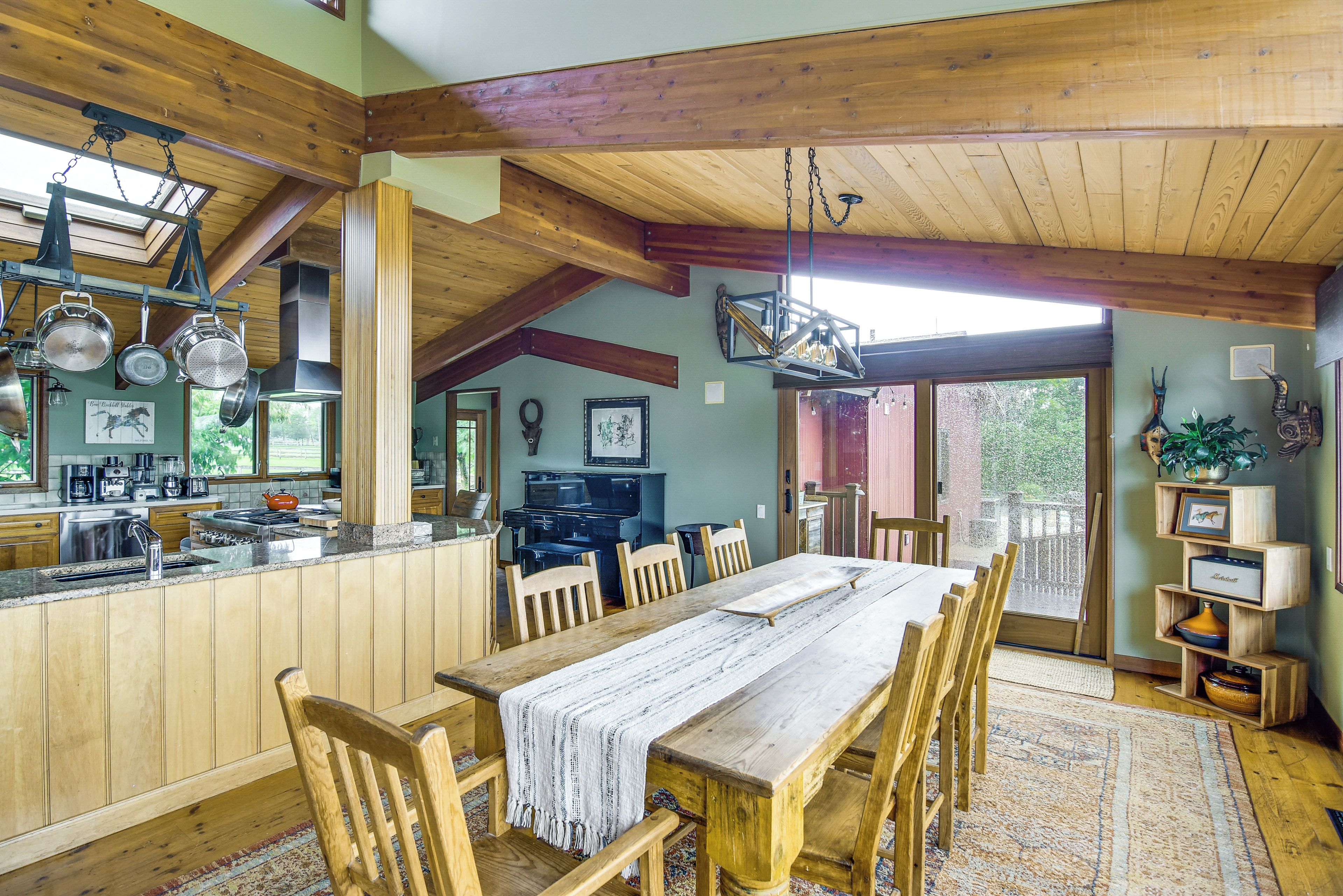 Une cuisine rustique avec des poutres en bois, un coin repas doté d’une grande table et une vue dégagée sur l’extérieur grâce à une porte vitrée.