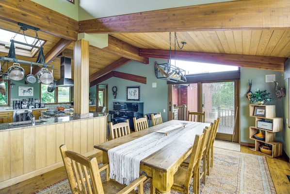 A rustic kitchen with wooden beams, a dining area with a large table, and a view through a glass door.