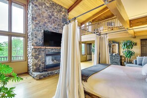 Une chambre spacieuse avec une cheminée en pierre, un grand lit et un balcon offrant une vue sur l’extérieur.