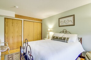A bedroom with a bed, a nightstand, a lamp, a framed picture on the wall, and a wooden wardrobe.