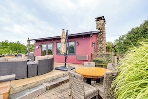A red building with a stone chimney, outdoor seating with wicker furniture, and a wooden fence.