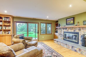 A living room with a stone fireplace, leather sofas, a bookshelf, and large windows.