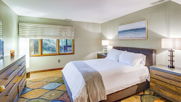 A bedroom with a bed, bedside tables, a dresser, a window with curtains, and a painting on the wall. - 6,000-sq-ft Estate in Delaware River Valley (Milford)
