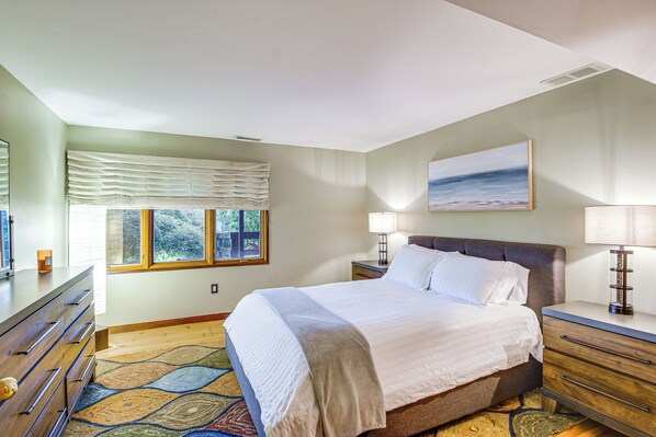 A bedroom with a bed, bedside tables, a dresser, a window with curtains, and a painting on the wall. - 6,000-sq-ft Estate in Delaware River Valley (Milford)