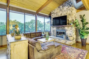 Un salon spacieux avec une cheminée en pierre, un canapé en cuir et de grandes fenêtres donnant sur la forêt.