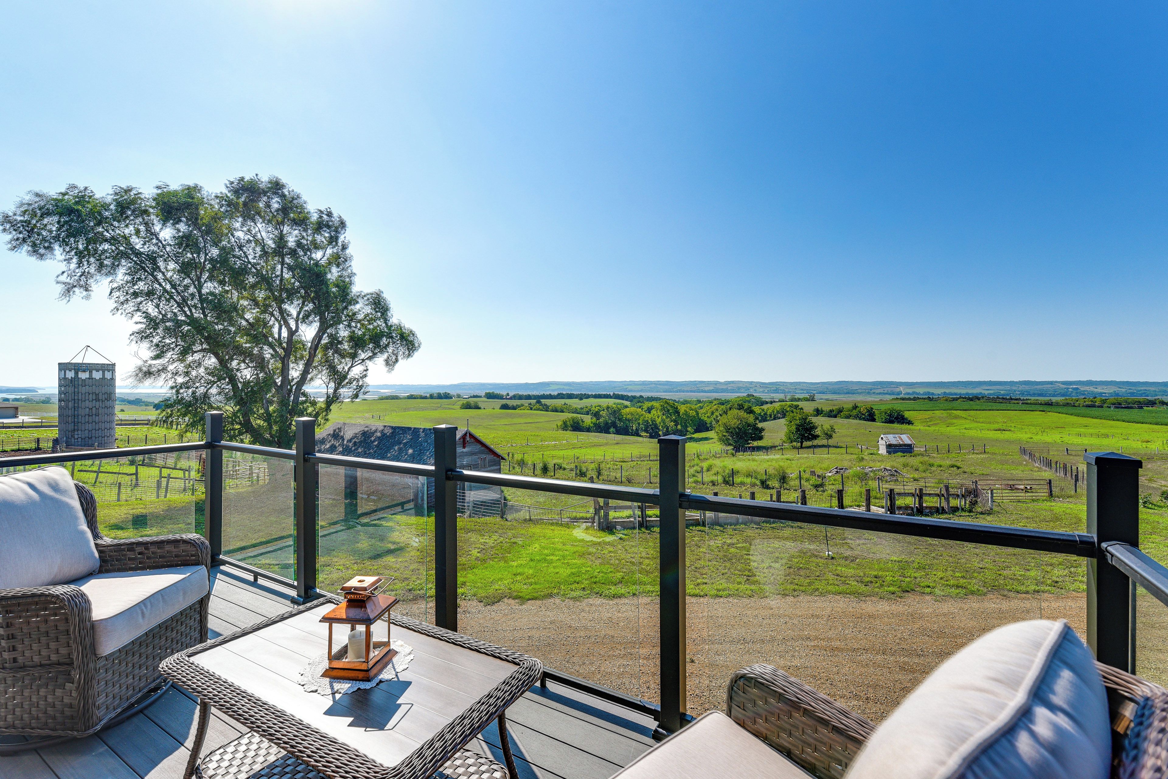 A balcony with wicker furniture, a lantern, and a view of a green landscape.