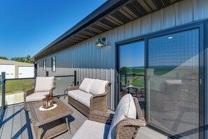 A covered outdoor seating area with wicker furniture and a table, overlooking a landscape.