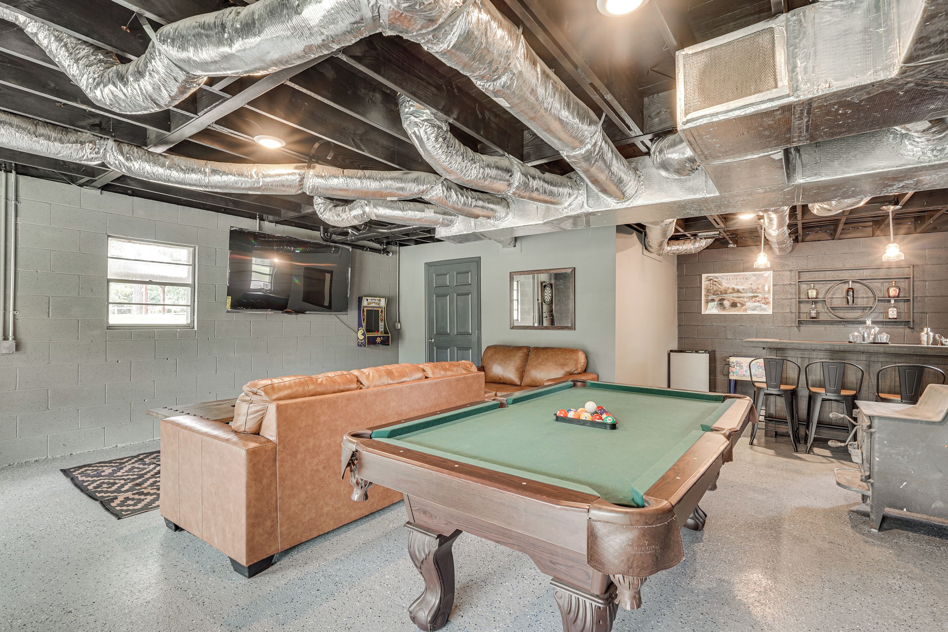 A pool table with a leather sofa and a billiards rack in a room with exposed ductwork and a brick wall.