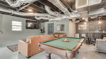 A pool table with a leather sofa and a billiards rack in a room with exposed ductwork and a brick wall.