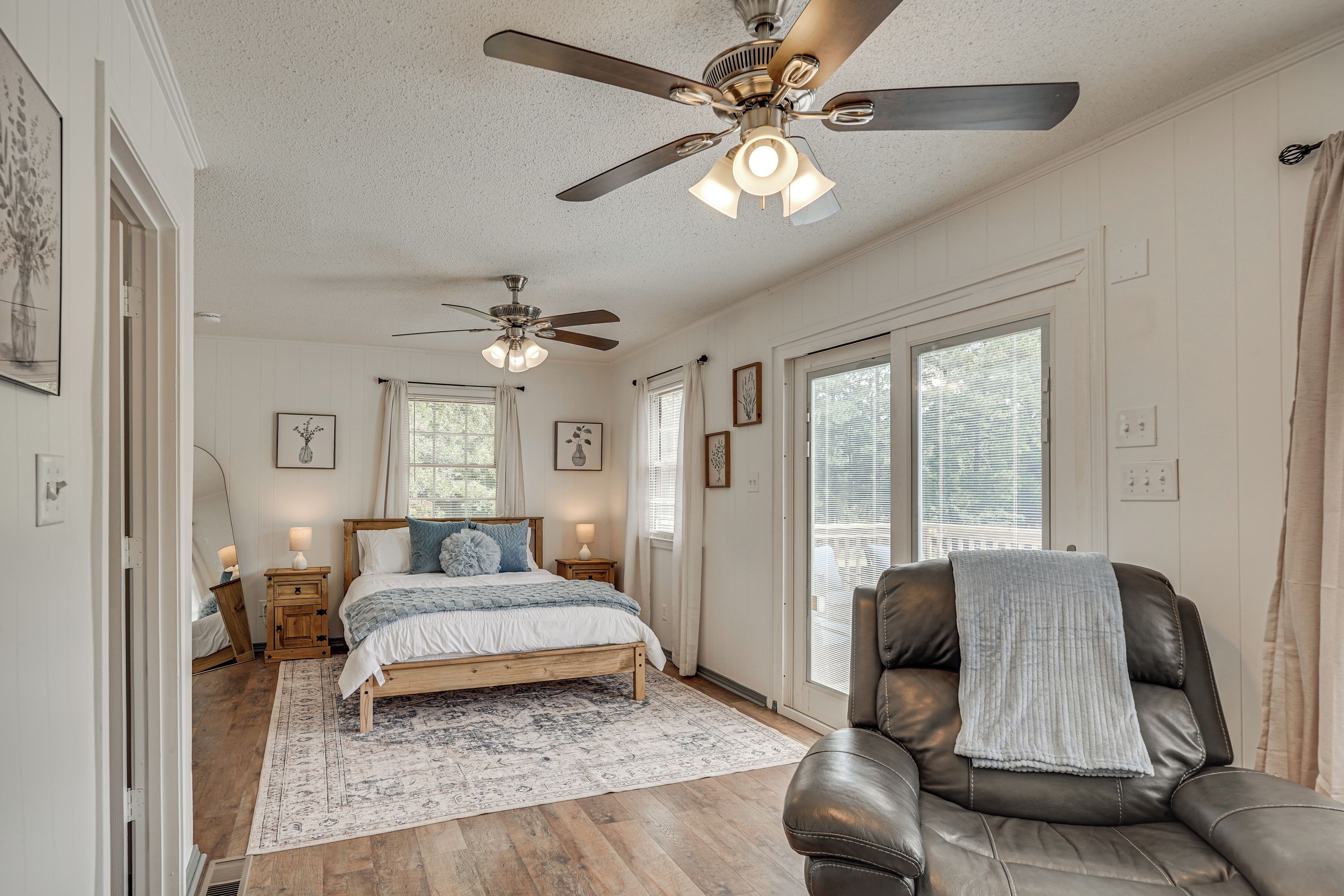 A bedroom with a bed, a chair, a ceiling fan, and a large window.