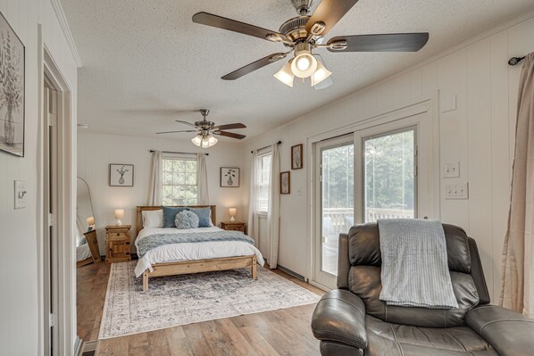 A bedroom with a bed, a chair, a ceiling fan, and a large window.