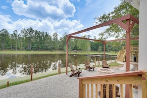 A deck with outdoor seating, a pond, and a forested area in the background. - Waterfront Retreat Near Masters Hot Tub & Sauna (Harlem)