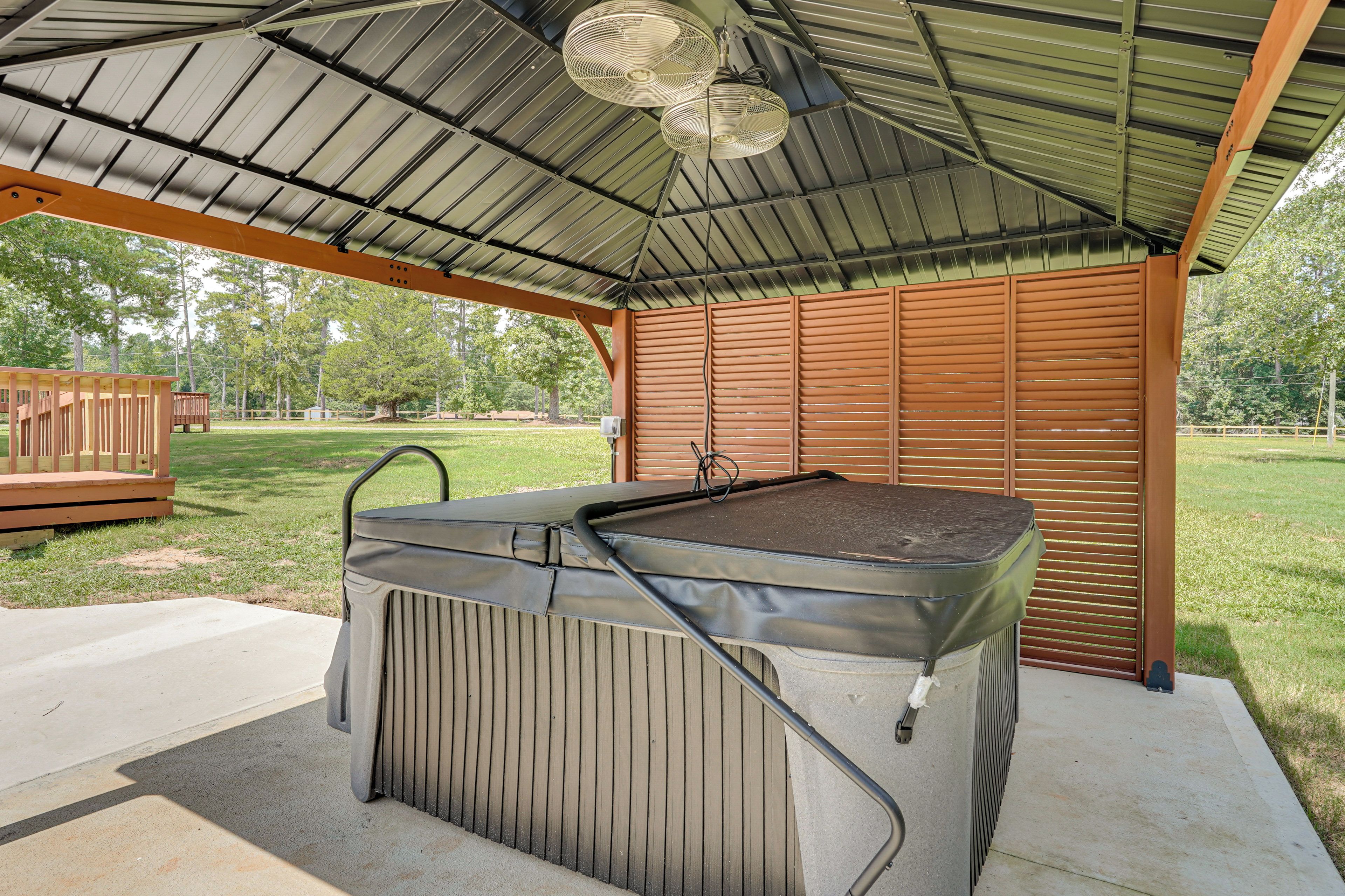 Eine überdachte Terrasse im Freien mit Whirlpool, Holzdeck und Metallveranda.