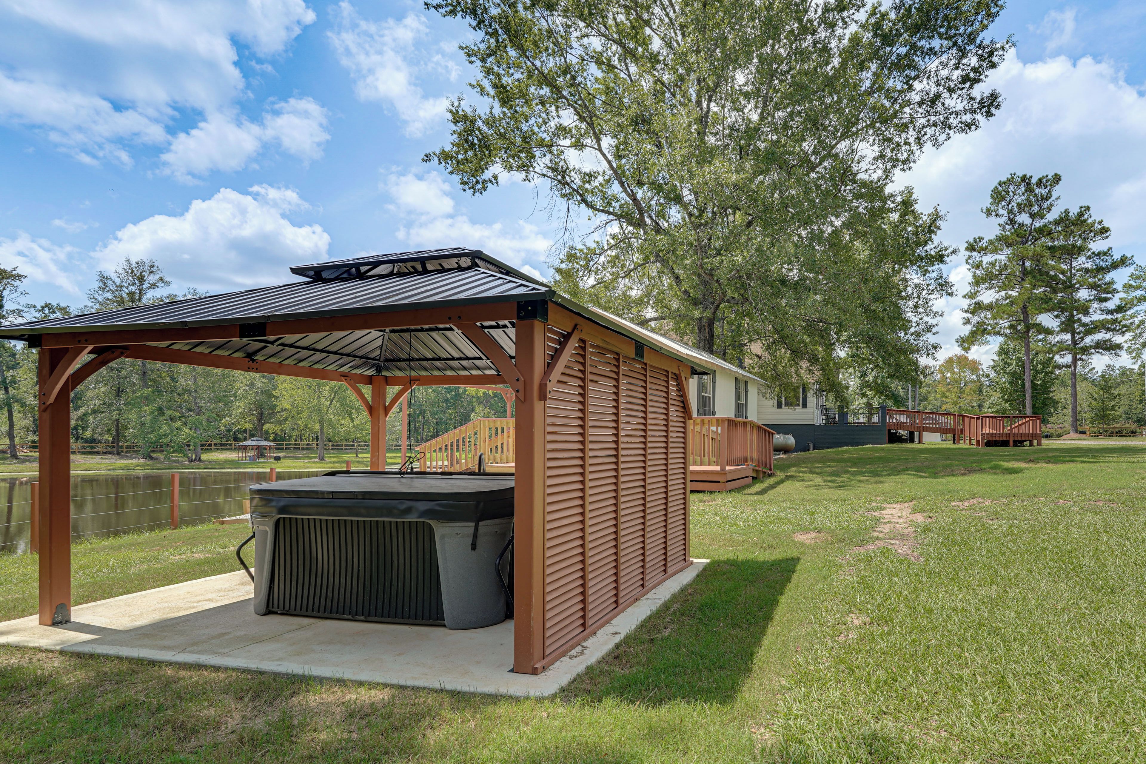 Un espacio al aire libre techado con un jacuzzi, una terraza de madera y vista a un lago.