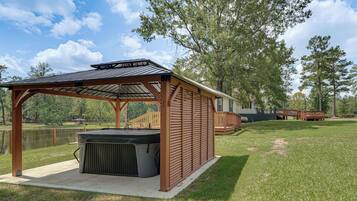 Un espacio al aire libre techado con un jacuzzi, una terraza de madera y vista a un lago.