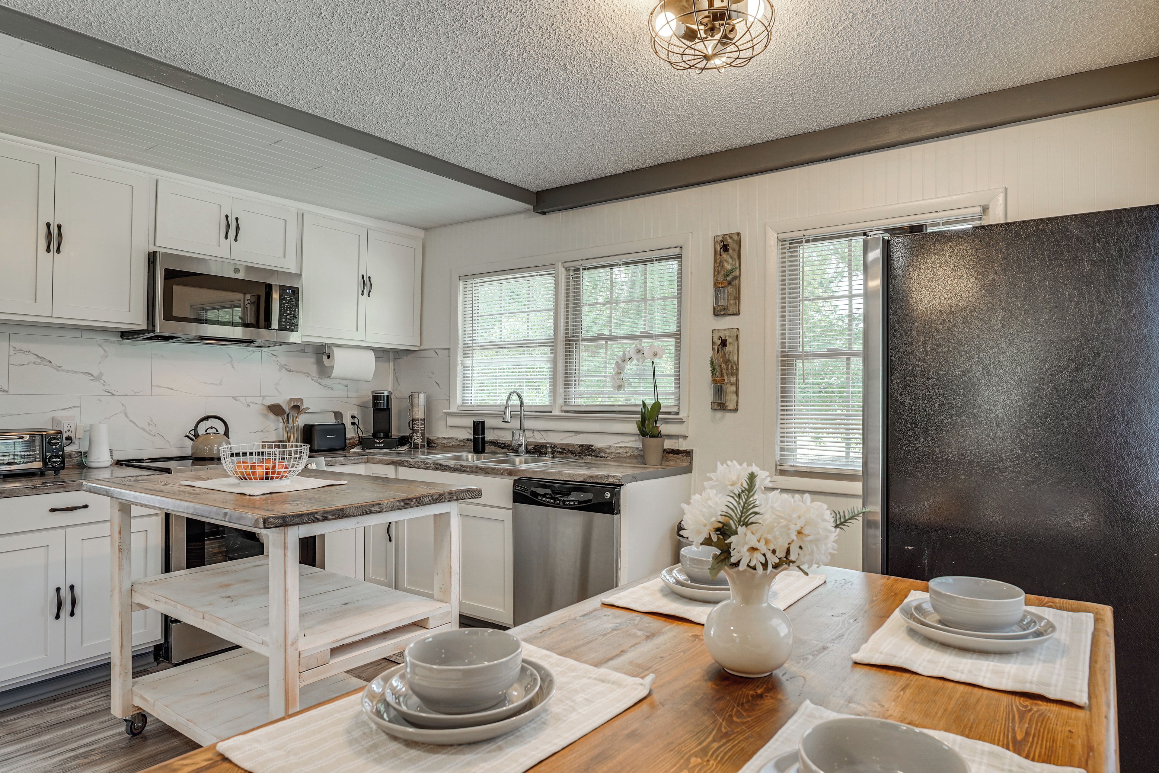 A modern kitchen with white cabinetry, a black refrigerator, and a wooden dining table set with bowls and plates.