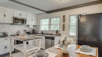 A modern kitchen with white cabinetry, a black refrigerator, and a wooden dining table set with bowls and plates.