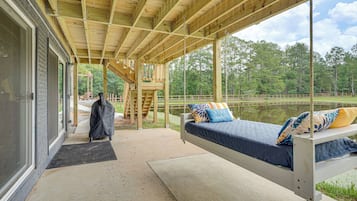 A covered outdoor seating area with a bed, a bench, and a view of a lake.