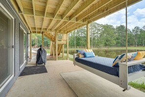 A covered outdoor seating area with a bed, a bench, and a view of a lake.