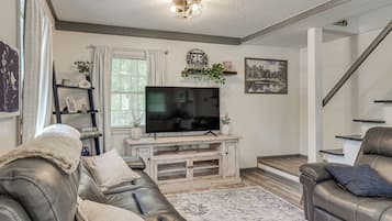 A living room with a flat-screen TV, leather sofas, a coffee table, and a staircase.