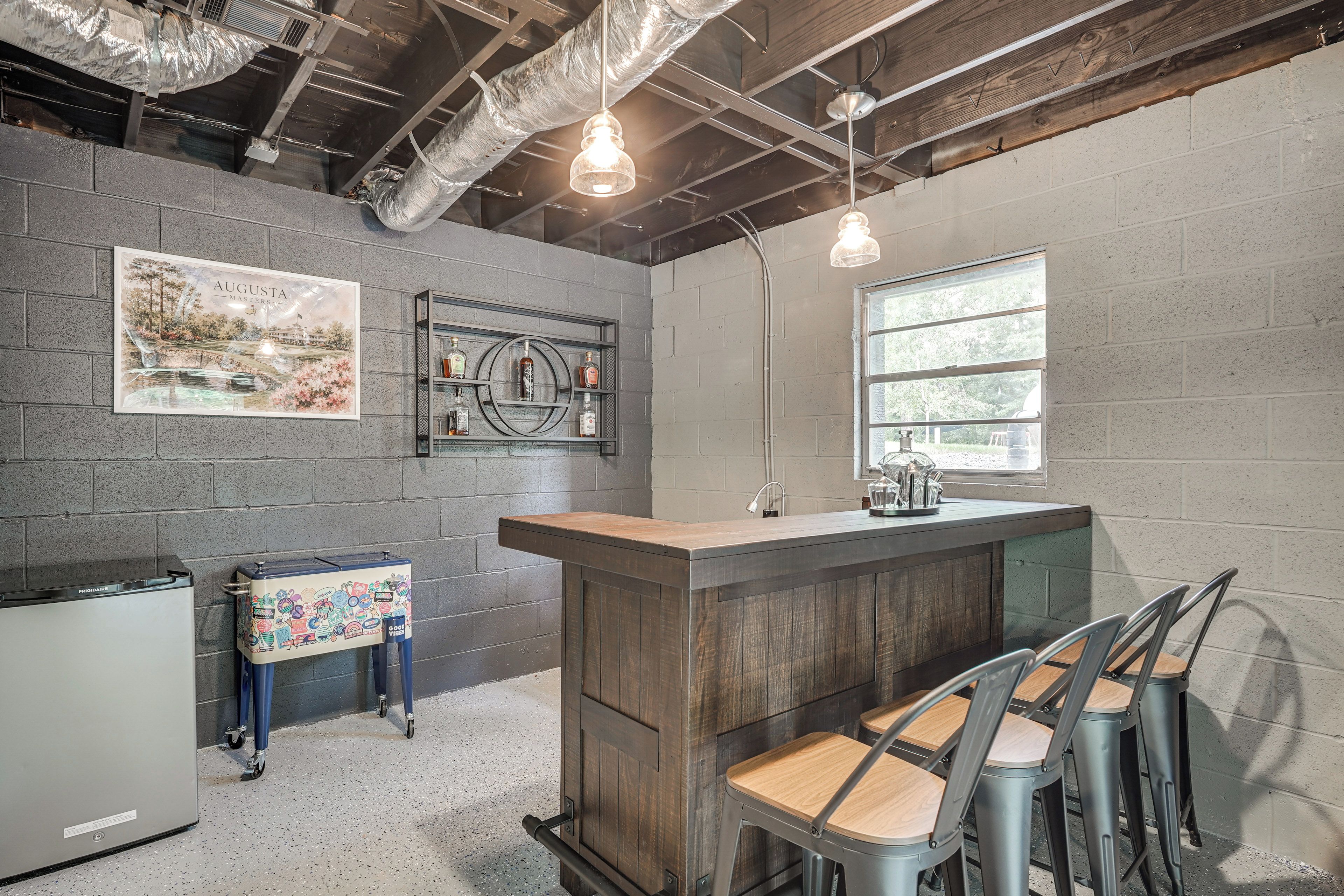 A bar area with a wooden counter, bar stools, a refrigerator, and a wall-mounted shelf with bottles.