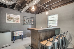 A bar area with a wooden counter, bar stools, a refrigerator, and a wall-mounted shelf with bottles. - Waterfront Retreat Near Masters Hot Tub & Sauna (Harlem)