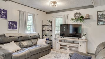 A living room with a leather sofa, a flat-screen TV, and decorative items on shelves.