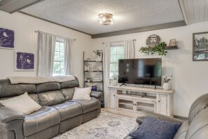 A living room with a leather sofa, a flat-screen TV, and decorative items on shelves.