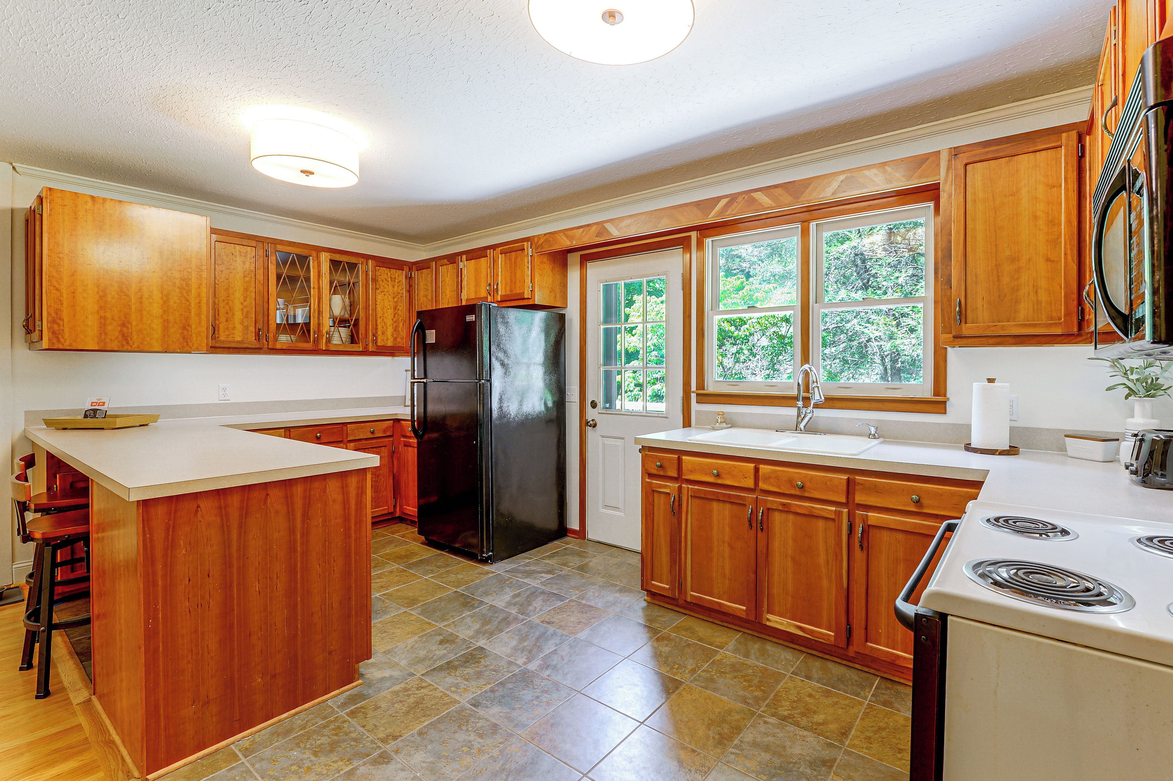 A kitchen with wooden cabinets, a black refrigerator, a sink, and a stove.